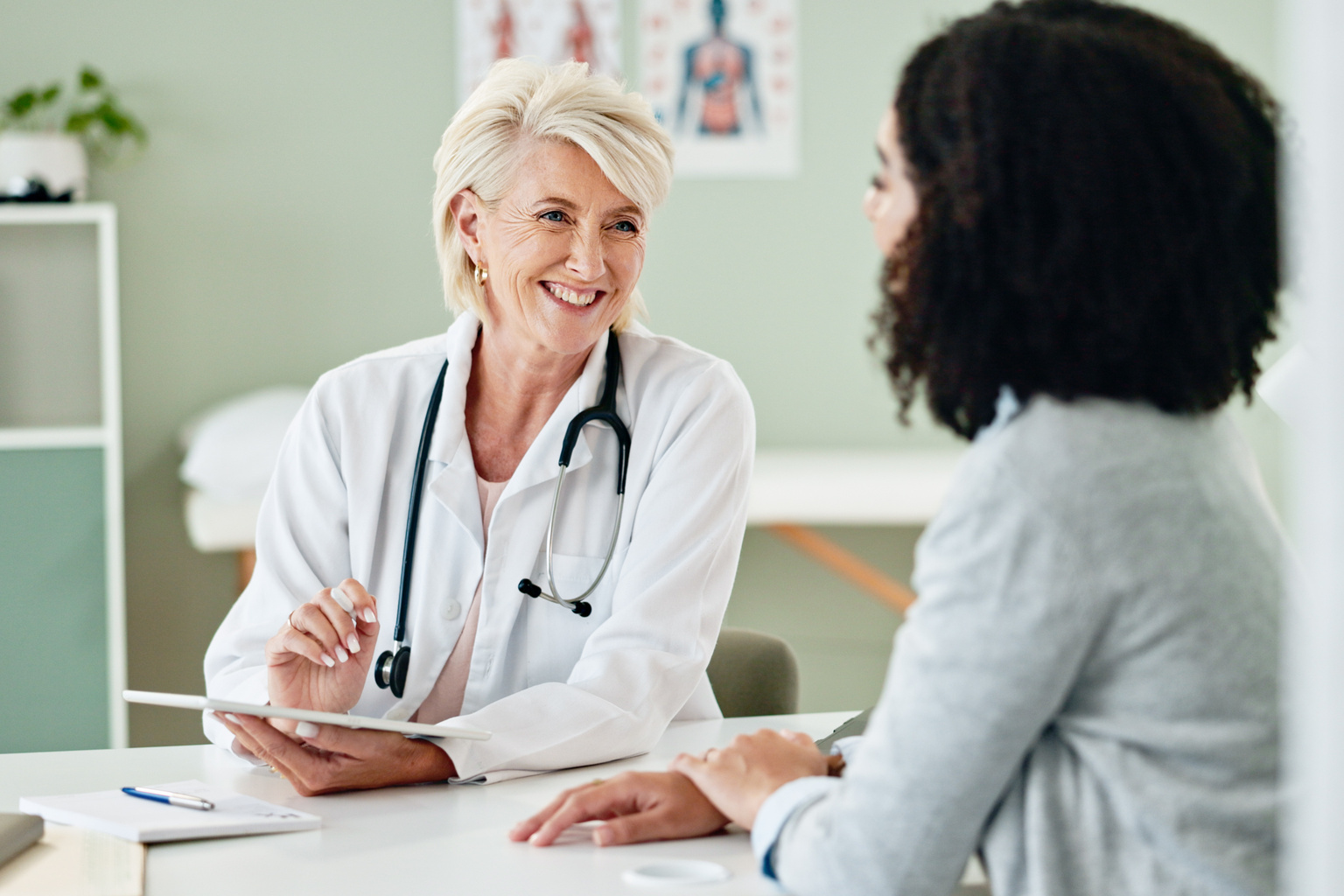 Mature doctor talking to patient in consultation with technology at clinic
