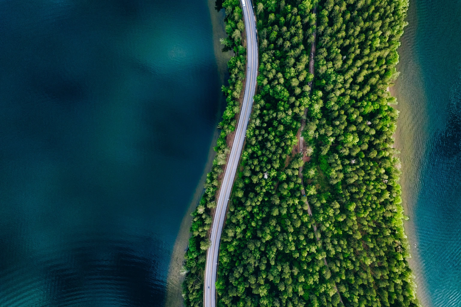 Aerial view of road between green forest and blue lake in Finland, 
