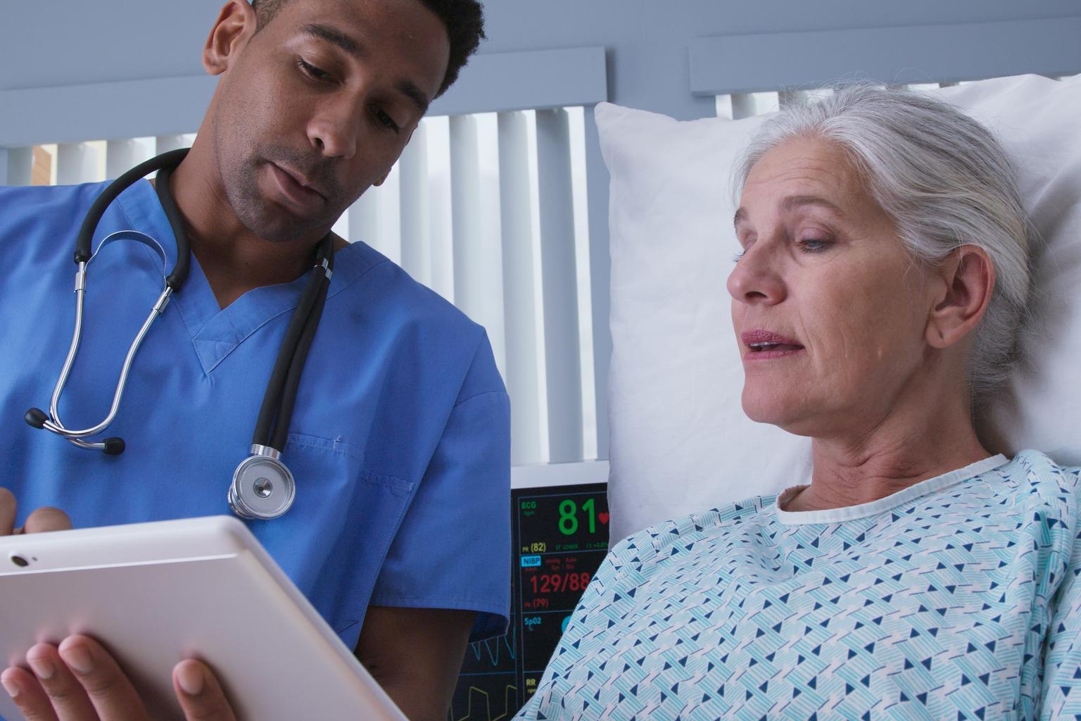 Male nurse with tablet and elderly female patient in hospital