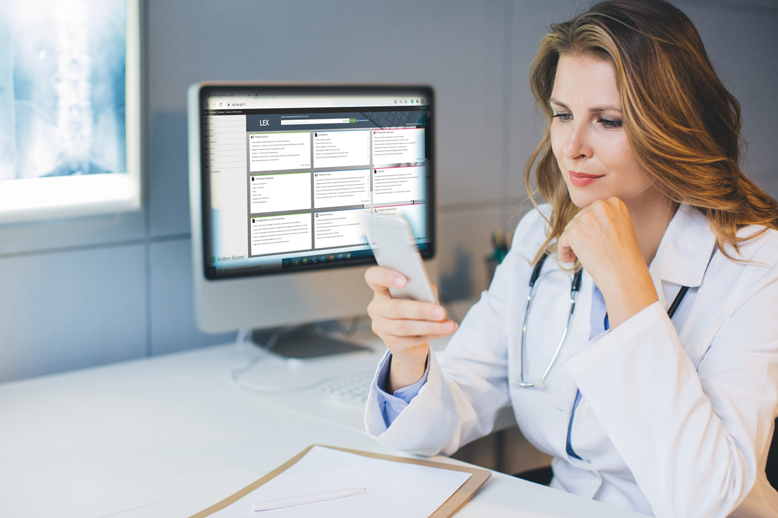 Lekarka patrzy na telefon, za nią jest komputer z LEX Compliance Medica